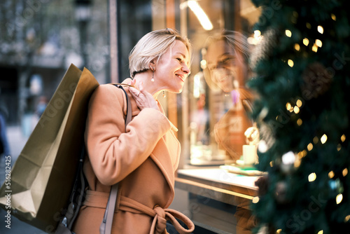 Beautiful woman with shopping bag looking through window of store