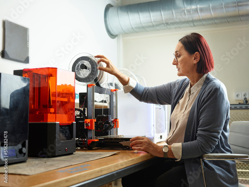Engineer adjusting filament of 3d printer at workshop