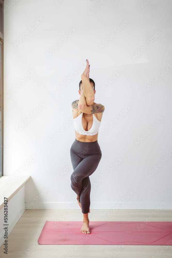 Woman practicing Garudasana on exercise mat in front of wall at yoga studio Woman practicing Garudasana on exercise mat in front of wall at yoga studio