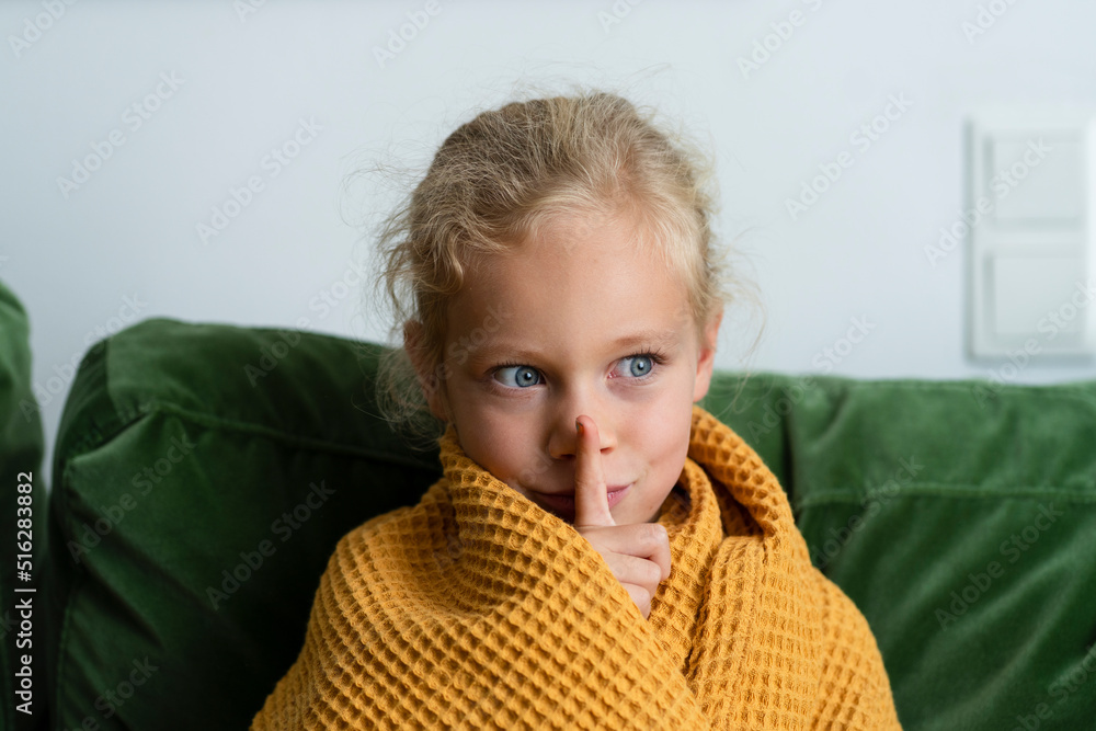 Contemplative girl wrapped in blanket making silence gesture at home Contemplative girl wrapped in blanket making silence gesture at home