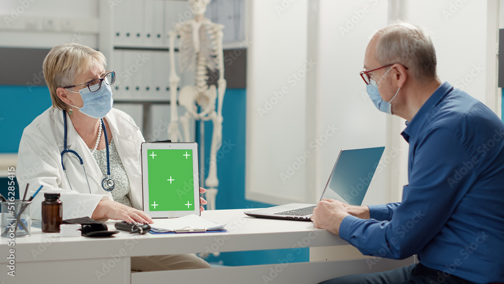 Physician showing digital tablet with greenscreen to old man in medical office during coronavirus pandemic. Blank isolated copyspace and mockup template with chroma key background. Physician showing digital tablet with greenscreen to old man in medical office during coronavirus pandemic. Blank isolated copyspace and mockup template with chroma key background.