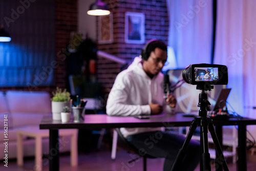 Modern person filming podcast episode on camera in studio, live broadcasting online discussion to create social media content. Male influencer vlogging show with livestream equipment.