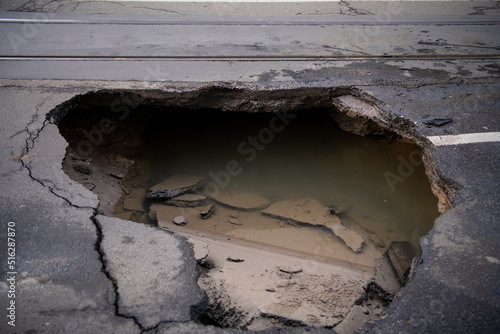 Huge sinkhole on busy asphalt road surface on which cars drive. Accident situation on a city street due to cracks in asphalt. Broken hole filled with muddy water. photo