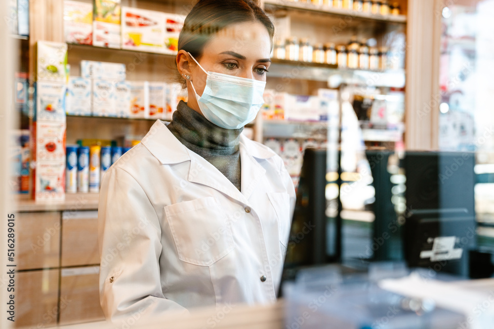 White apothecary wearing lab coat and face mask working with till White apothecary wearing lab coat and face mask working with till
