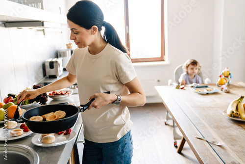 Smiling young mother cooking breakfast in the kitchen