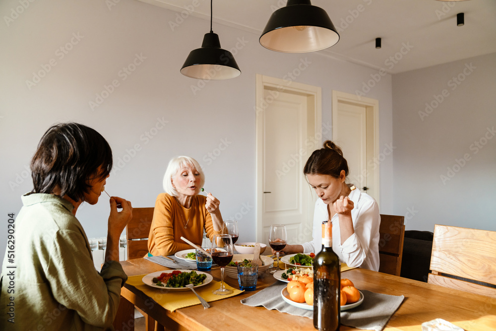 Mature three women smiling and talking while having lunch together Mature three women smiling and talking while having lunch together