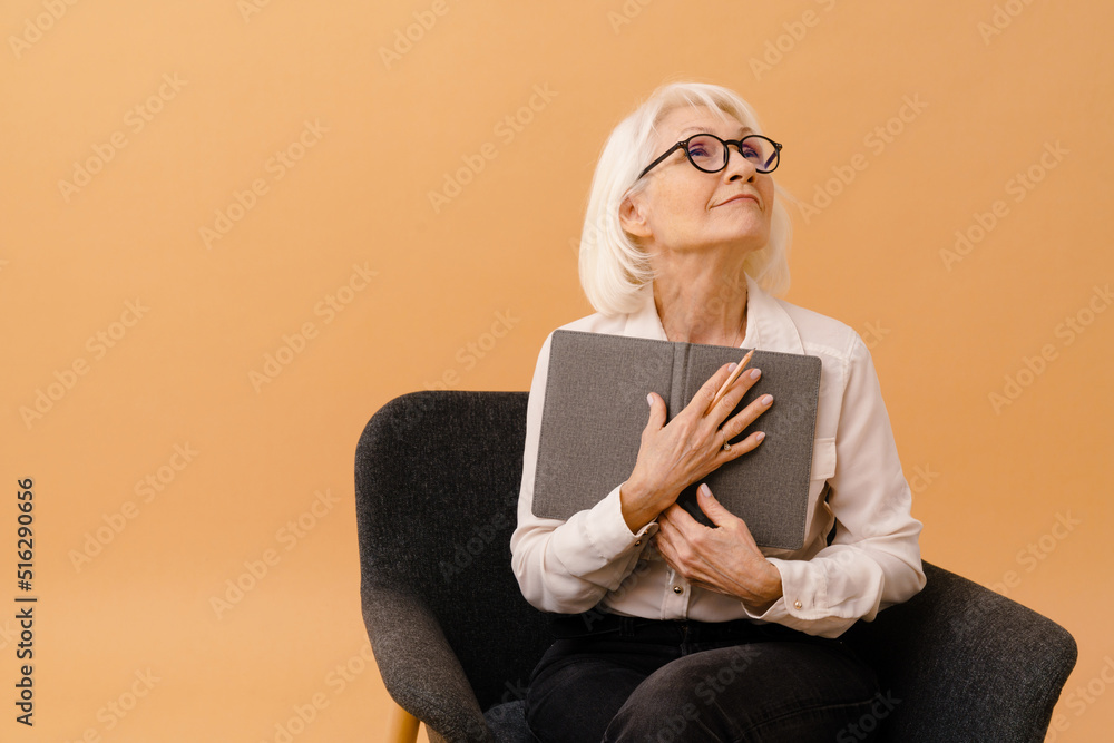 Beautiful senior woman in business suit writing notes on armchair Beautiful senior woman in business suit writing notes on armchair