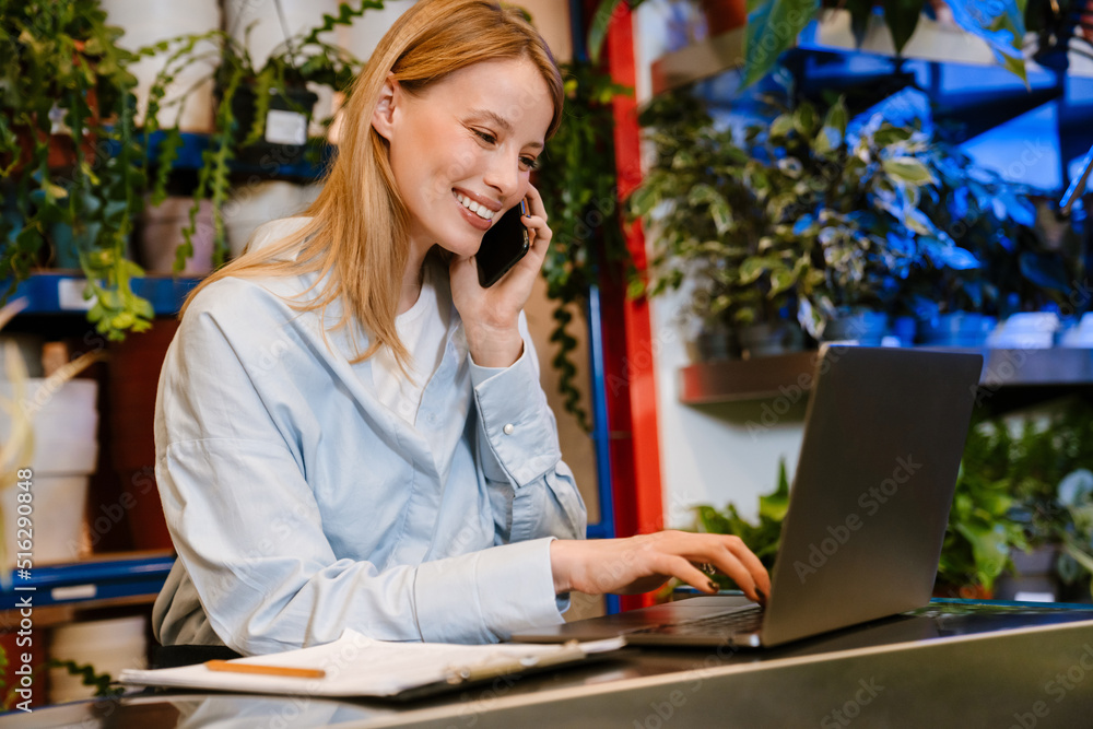 Florist girl talking on cellphone and using laptop in plant store Florist girl talking on cellphone and using laptop in plant store