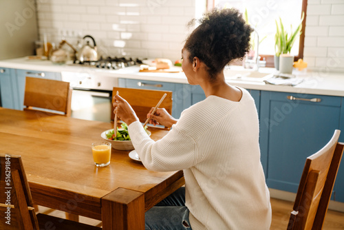 Tableau sur toile Back view of african woman sitting by table eating salad