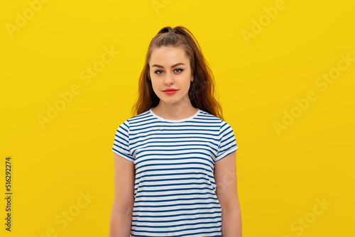 cute beautiful young woman with dark hair wearing striped t shirt, looking at camera and pleasantly smiling, standing over yellow background