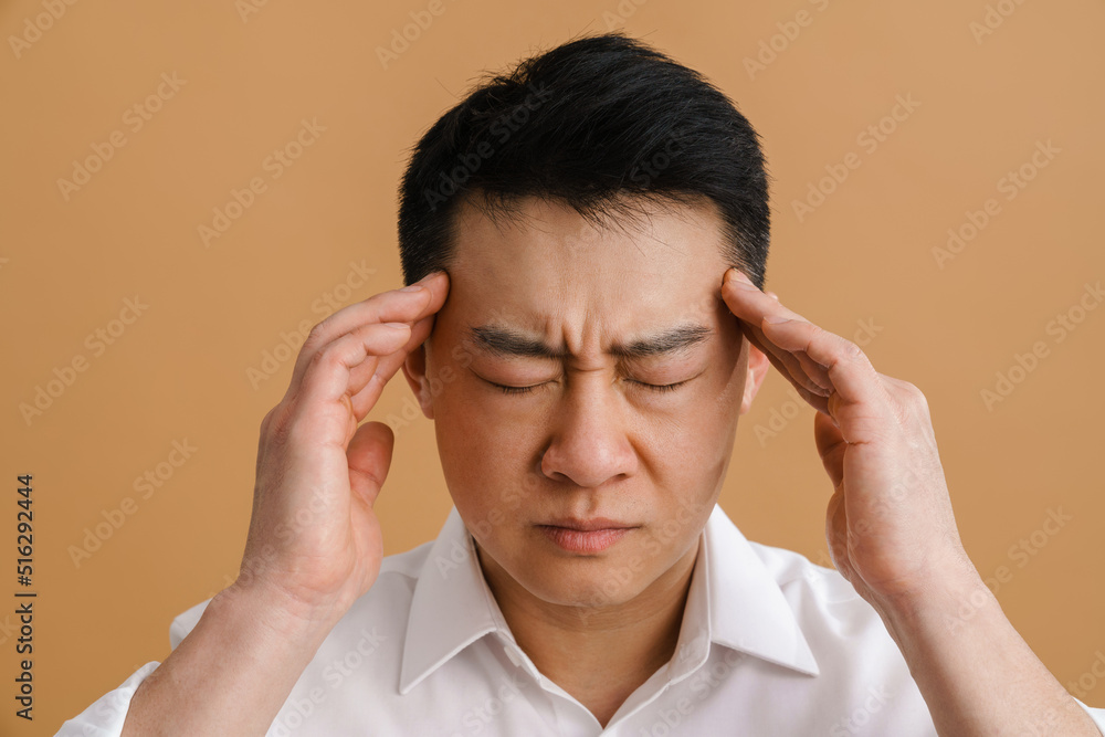 Brunette adult asian man wearing shirt rubbing his temples