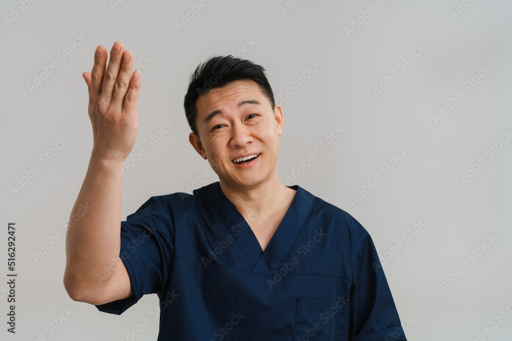 Adult asian man wearing medical uniform smiling and raising his hand Adult asian man wearing medical uniform smiling and raising his hand