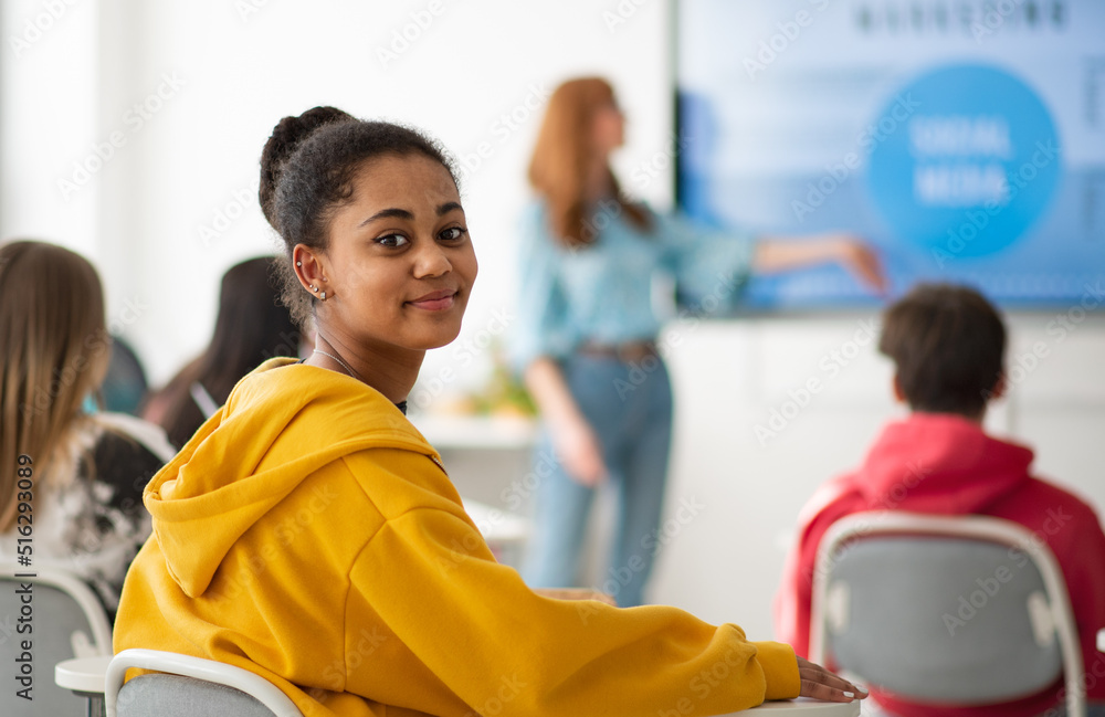 College student sitting in school-desk and looking at camera. - obrazy, fototapety, plakaty 