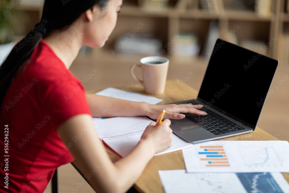 Busy concentrated teen asian lady study at table with laptop with empty screen, watch online lesson in room Busy concentrated teen asian lady study at table with laptop with empty screen, watch online lesson in room