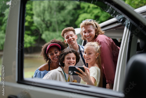 Multiracial young friends travelling together by car, taking selfie - summer vacation, holidays, travel, road trip and people concept. © Halfpoint