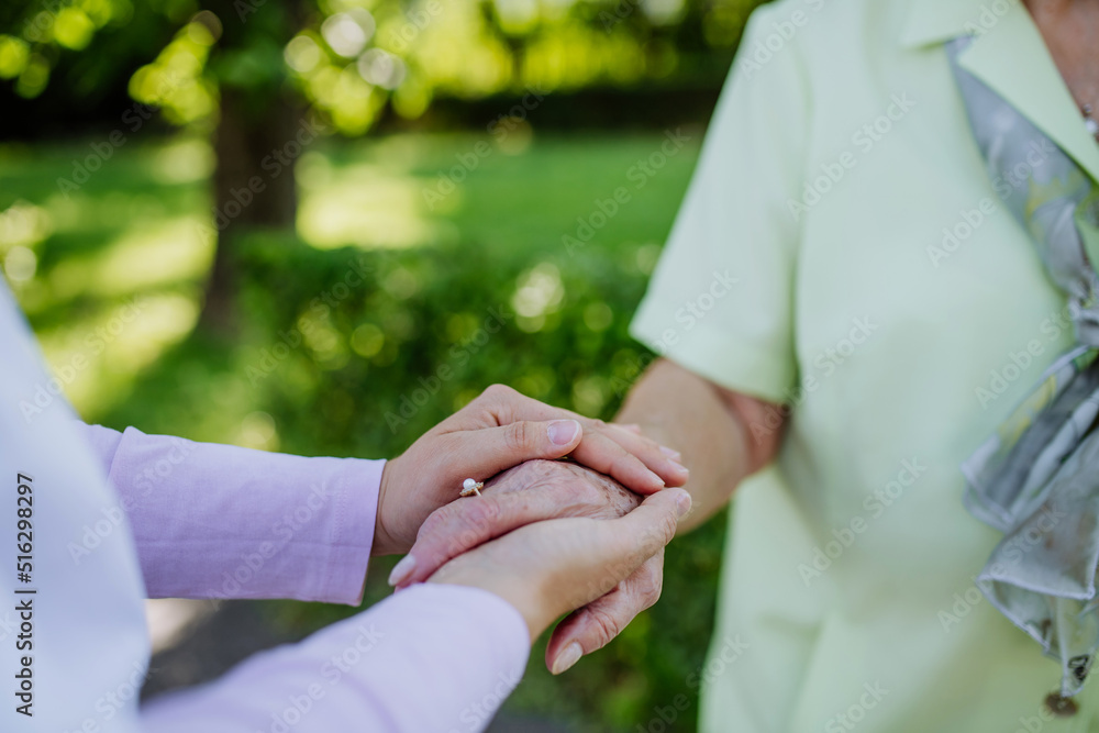 Close-up of caregiver consoling senior woman and touching her hand in park in summer. Close-up of caregiver consoling senior woman and touching her hand in park in summer.