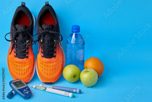 Orange sneakers, fruits, glucometer, insulin syringe pens and plastic drinking water bottle on a blue background. Exercise, nutrition and diabetes management
