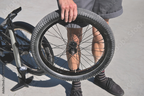 boy holds a bmx bicycle wheel in his hand against the background of a pump and a bike during repair and maintenance