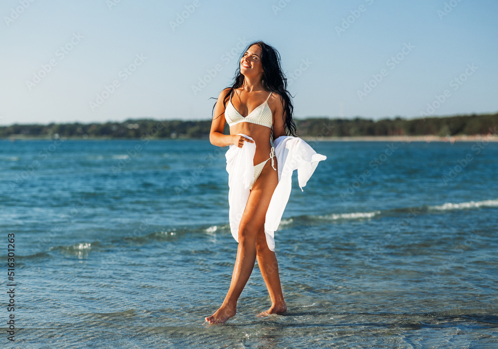 Naklejka premium people, summer and swimwear concept - happy smiling young woman in bikini swimsuit with pareo on beach