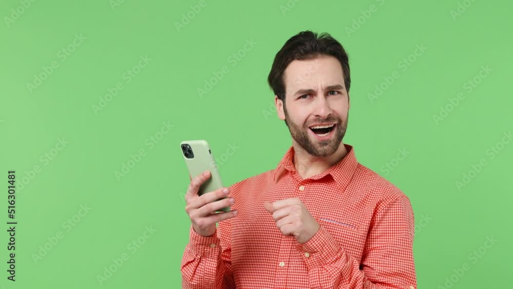 Happy young brunet bearded man 20s wear pink shirt hold use mobile cell phone typing browsing swipe chatting send sms doing online shopping booking tour isolated plain green background studio portrait Happy young brunet bearded man 20s wear pink shirt hold use mobile cell phone typing browsing swipe chatting send sms doing online shopping booking tour isolated plain green background studio portrait