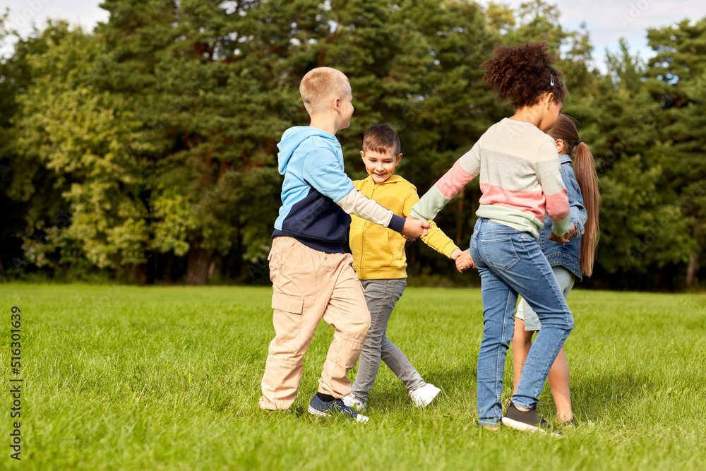 childhood, leisure and people concept - group of happy kids playing round dance at park childhood, leisure and people concept - group of happy kids playing round dance at park