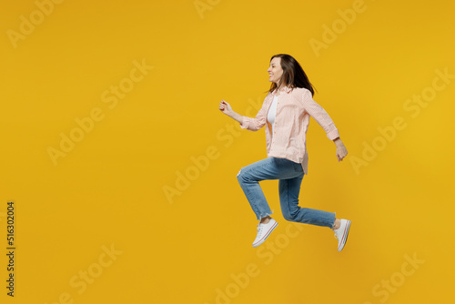 Full body side view young happy sporty fun woman she 30s wears striped shirt white t-shirt jump high run fast hurry up isolated on plain yellow background studio portrait. People lifestyle concept