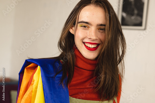 Image of happy caucasian non-binary trans woman with rainbow fabric photo