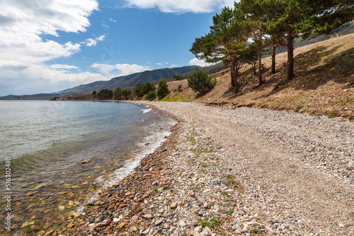 Summer landscape of the shore of Baikal Lake with a pebble beach and coniferous trees on the coast of the Small Sea on a sunny day