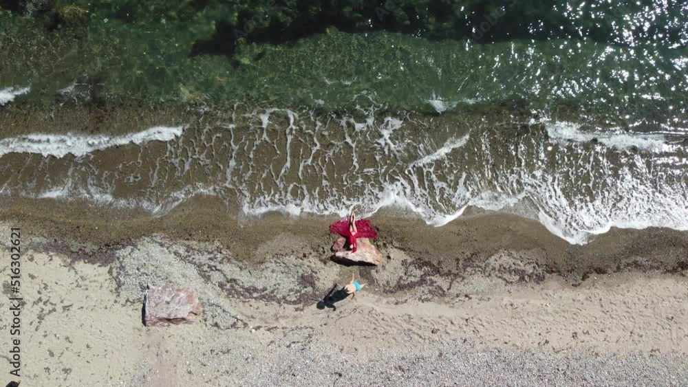 Top aerial view on a young sensual blonde woman in red bikini lying on the rock near water at sea and enjoys the sea waves. Dreams holidays and weekend vacation in summer time. Top aerial view on a young sensual blonde woman in red bikini lying on the rock near water at sea and enjoys the sea waves. Dreams holidays and weekend vacation in summer time.