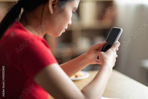 Disappointed adolescent asian girl female chatting in social networks on smartphone with empty screen