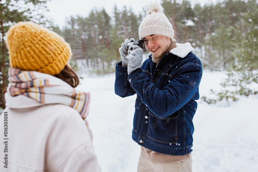 people, love and leisure concept - happy smiling man photographing woman in winter forest