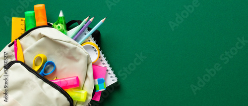Obraz na plátně Backpack with colorful school supplies on green background