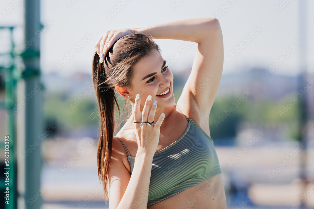 Cheerful italian brunette girl at sport court in bra making ponytail  looking aside. Exhausted spanish girl at her morning training having break.  Fitness and health care. Happy european girl training. Stock Photo