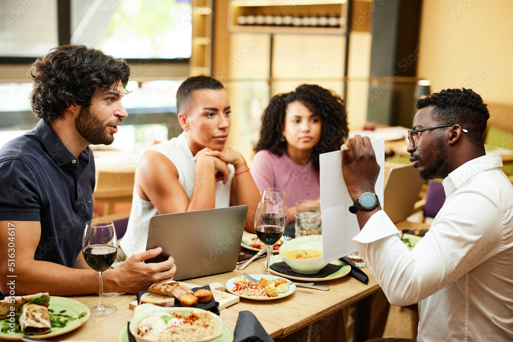 An African casual businessman has a presentation for his colleagues at the dinner table in a restaurant. An African casual businessman has a presentation for his colleagues at the dinner table in a restaurant.