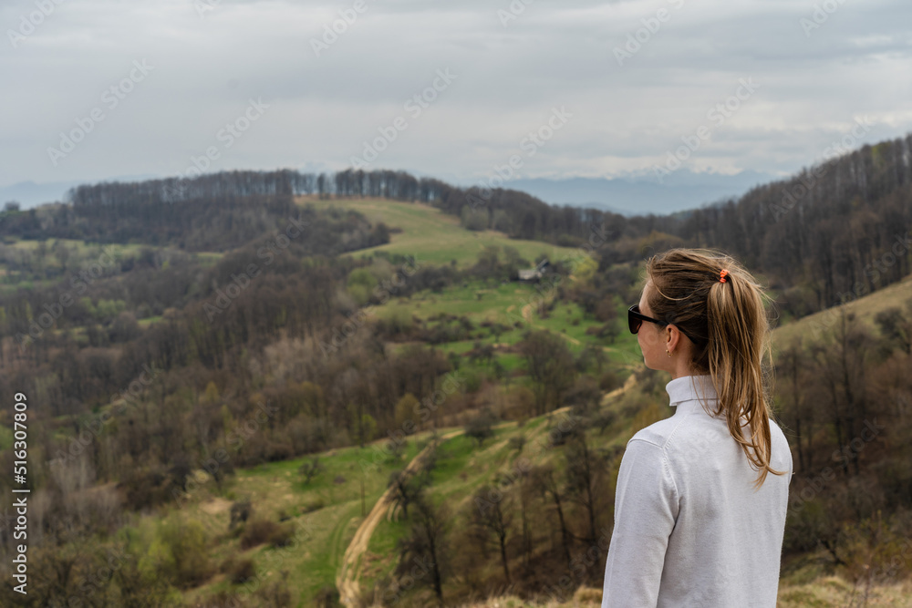 Naklejka premium Beautiful mountains and standing young woman on top hills. Landscape with mountain peak, forest. Travel concept