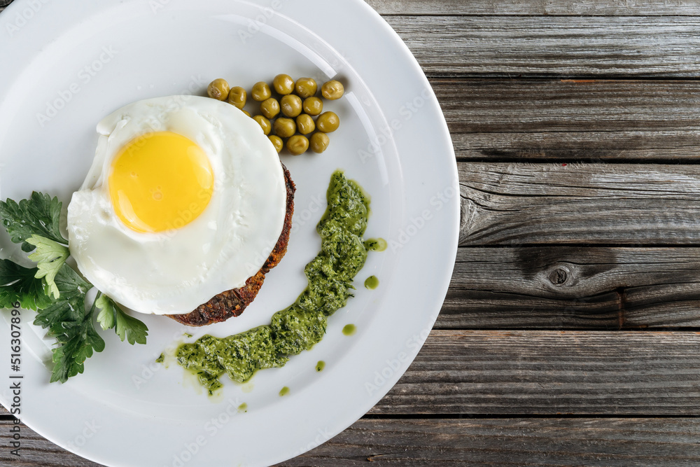 Scrambled eggs with meat on a plate, garnished with green peas and pesto sauce.