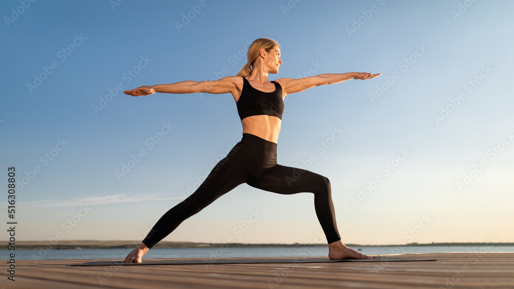 Fototapeta premium Beautiful Middle Aged Woman Practicing Yoga Outdoors, Standing In Warrior Pose