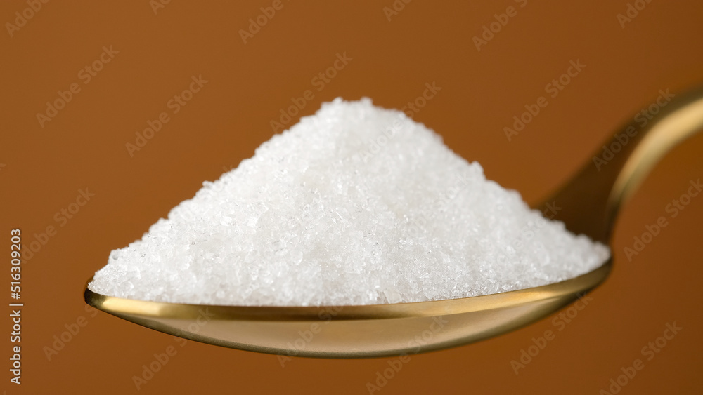 White sugar in golden spoon, close up