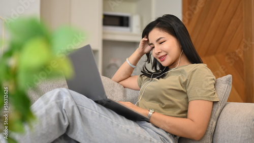 Asian female freelancer working online, surfing internet on laptop while relaxing in cozy living room