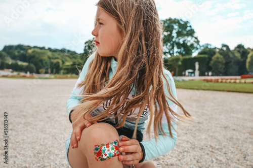 A little girl child fell and hurt her leg. The wound on the knee is sealed with a band-aid.