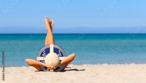 Fototapeta Naklejka Na Ścianę i Meble -  A slender girl on the beach in a straw hat in the colors of the Martinique flag. The concept of a perfect vacation in a resort in the Martinique. Focus on the hat.
