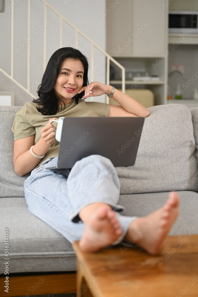 Casual young woman drinking herbal tea and using laptop in modern home Casual young woman drinking herbal tea and using laptop in modern home
