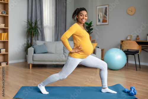 Cheerful young pregnant black woman athlete with big belly doing leg exercises and practicing yoga