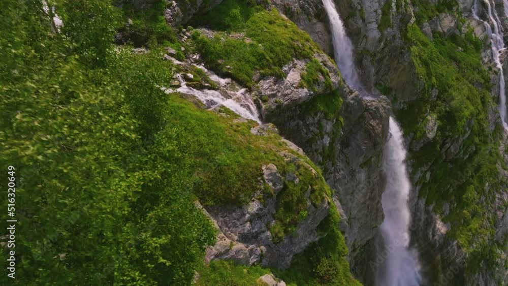 Aerial view close up flight with mountain waterfalls flowing from glacier over rocks. Fall of water in a green mountain gorge. Movement in three axes Aerial view close up flight with mountain waterfalls flowing from glacier over rocks. Fall of water in a green mountain gorge. Movement in three axes