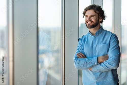 Portrait of confident mature businessman standing near window in modern company office, copy space