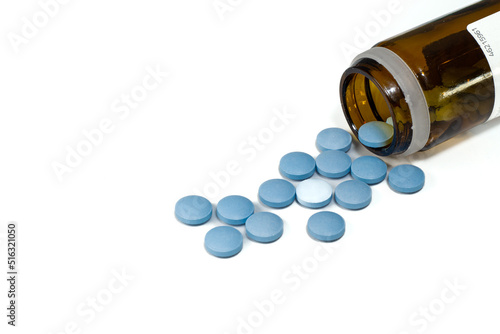 glass bottle with scattered blue pills on white background photo