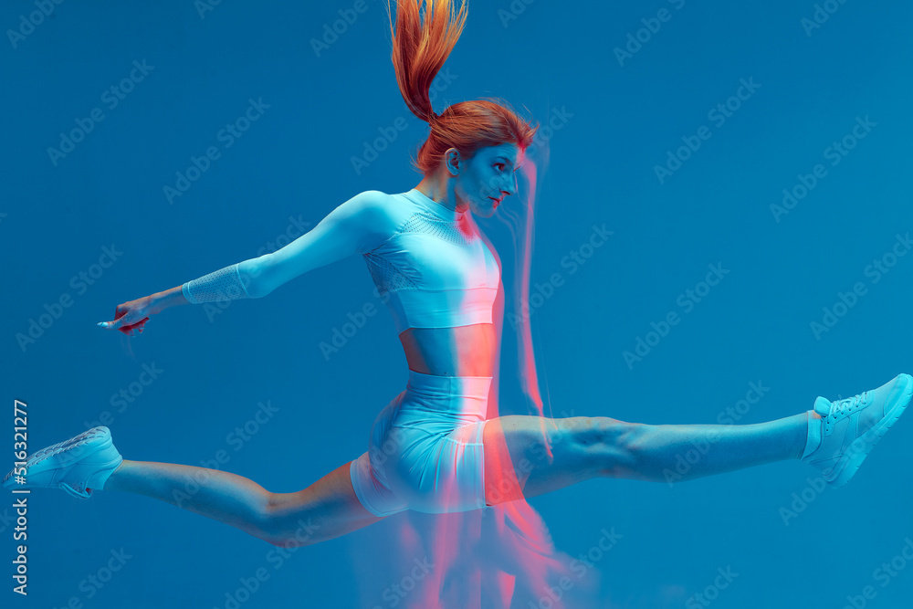 Girl jumps in white sport suit on a blue background. Isolated fitness model. High jump with blur effect.