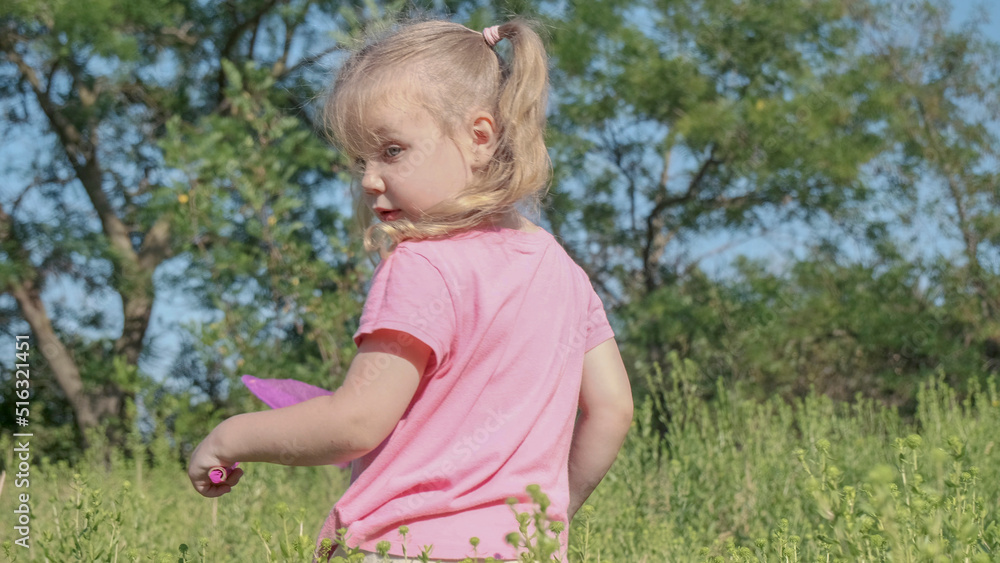 Little girl plays with butterfly net of tall grass in city park. Cute little girl is playing with aerial insect net in meadow on sun day. Little girl plays with butterfly net of tall grass in city park. Cute little girl is playing with aerial insect net in meadow on sun day.