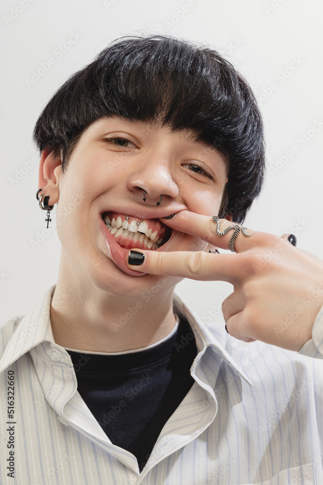 Close-up portrait of stylish young man with piercing, making faces, posing isolated over grey studio background. Extraordinary look Close-up portrait of stylish young man with piercing, making faces, posing isolated over grey studio background. Extraordinary look