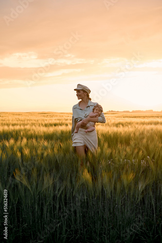 A portrait of young mother with a baby in her arms at sunset in the field. happy family concept